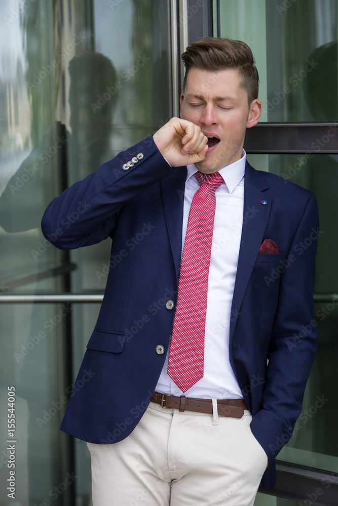 blond man in suit leaning against window and yawning blond man in suit leaning against window and yawning