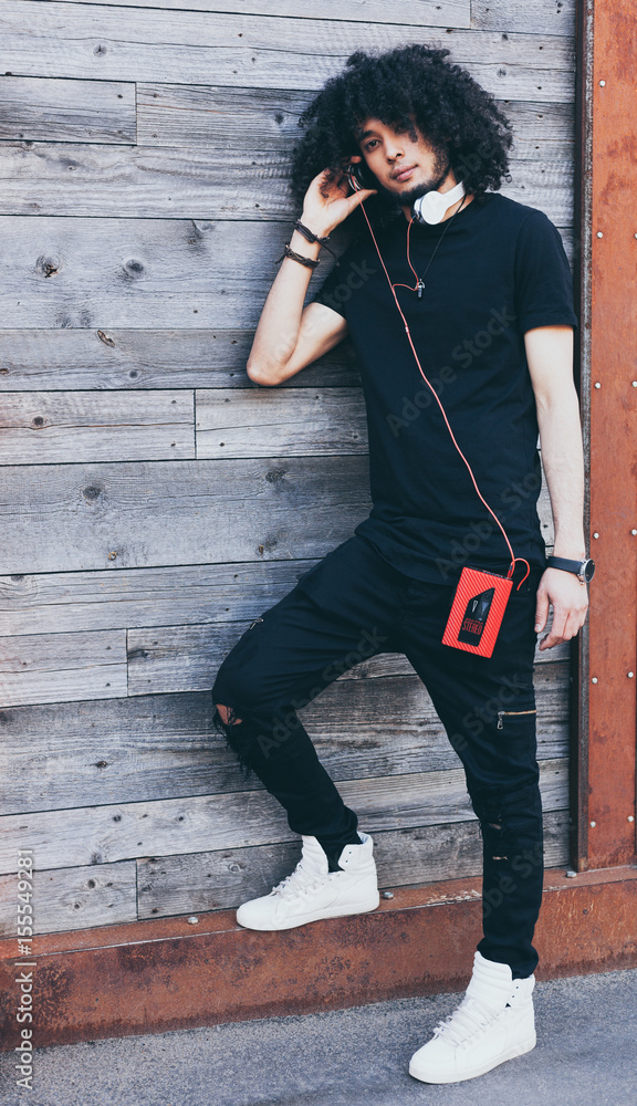 African American man with an afro hairstyle listens to music as DJ,  resting. Headphones and vintage cassette player. Wearing a black outfit and  high white sneakers. Rockstar. Reggae. Stock Photo | Adobe