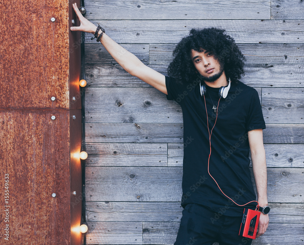 Young African American man with an afro hairstyle as DJ posing on wooden  background. Headphones and red vintage cassette player. Wearing a black  outfit. Rockstar. Reggae. Stock Photo | Adobe Stock