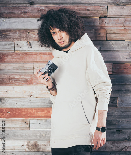 African american man with afro hair posing with vintage camera on colourful background of old boards. Dressed in a cool white outfit. Afrohair. photo