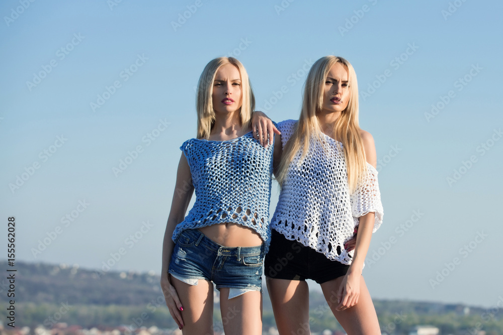 Twin sisters, sexy girls, posing on blue sky Photos Adobe Stock