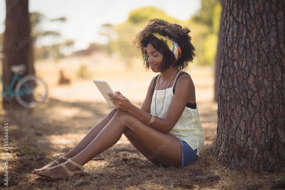 Young woman using digital tablet while sitting by tree