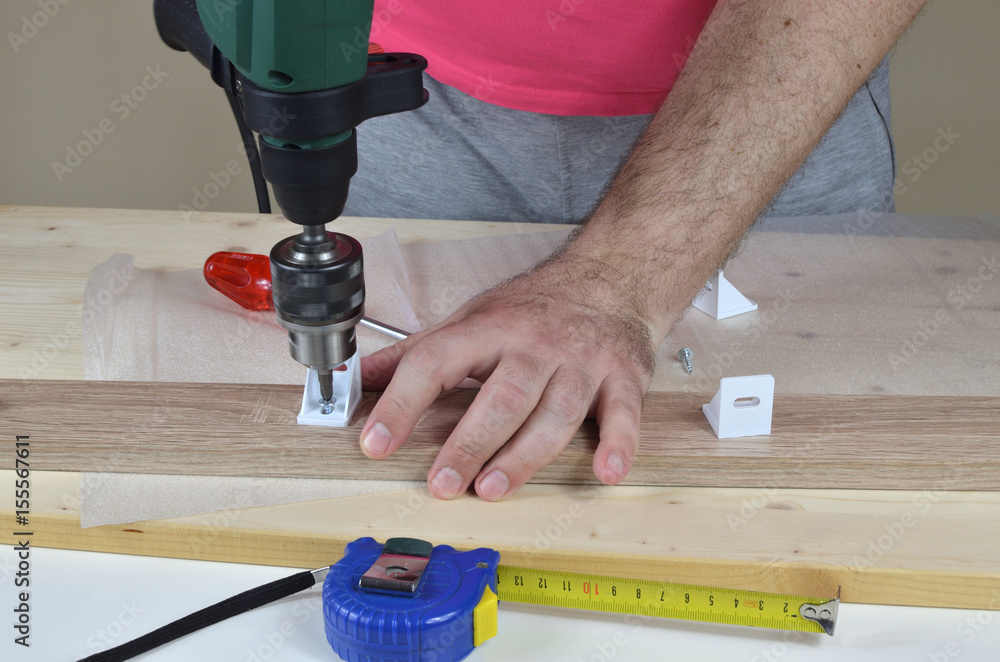 Man holding an electric screwdriver and installing elements of a cabinet