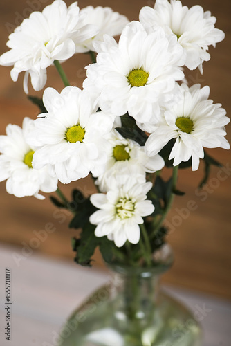 Wallpaper Mural Close-up of flowers in a glass vase with water on wooden background. Daisy flower. Vertical shoot. Torontodigital.ca