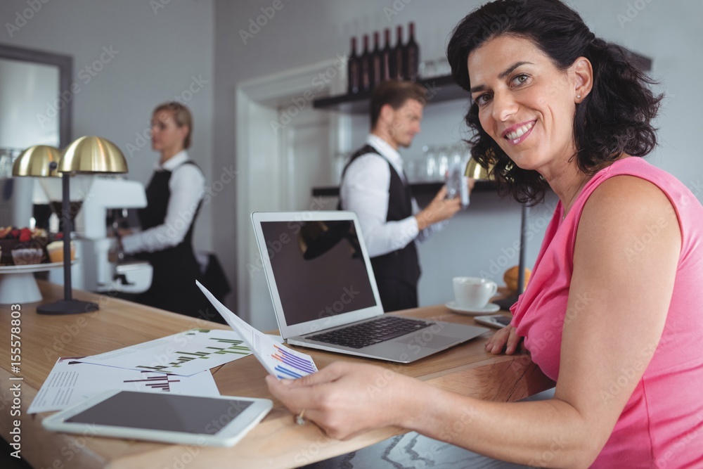 Smiling woman working with graph chart and laptop at bar counter