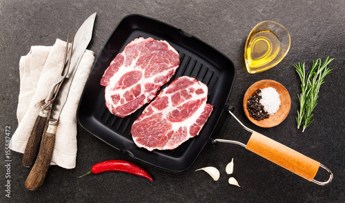 raw steak in a frying pan for the grill on stone background with cutting Cutlery for slicing and spices