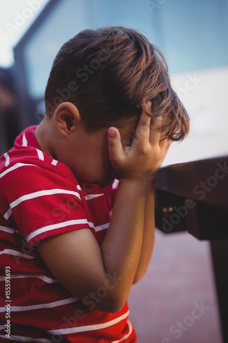 Close up of boy with hands covering face sitting at table
