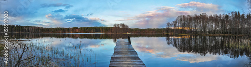 Panorama landscape. Wooden pier on the lake at sunset, clouds reflection in the water.