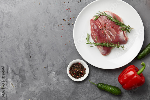 Raw duck breast in white plate with vegetables on gray stone background