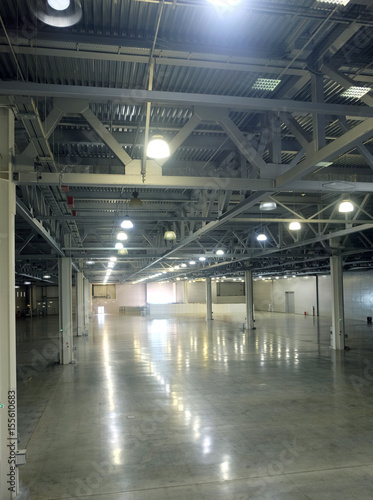 Large empty warehouse interior in an industrial building with high vertical columns with and high ceiling and artificial lighting