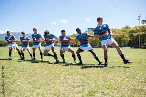 Rugby players pulling rope while standing on grassy field
