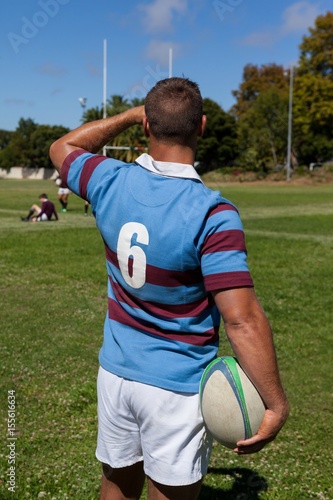 Rear view of player holding rugby ball at playing field