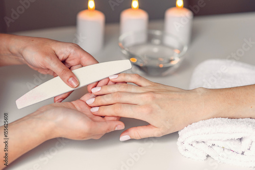 Spa salon. Beautiful woman hands having nail filing with nail file by manicurist. Cosmetic procedure, manicure on female hand