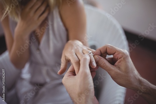 Man putting engagement ring on woman's hand photo