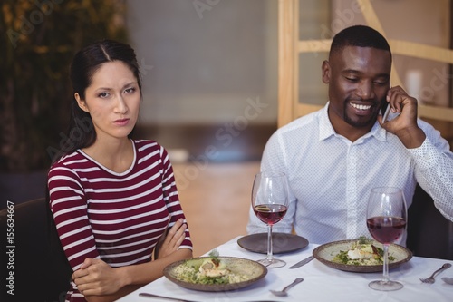 Man ignoring bored woman while talking on mobile phone