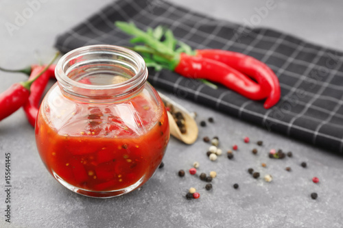 Jar with tasty chili sauce on grey table