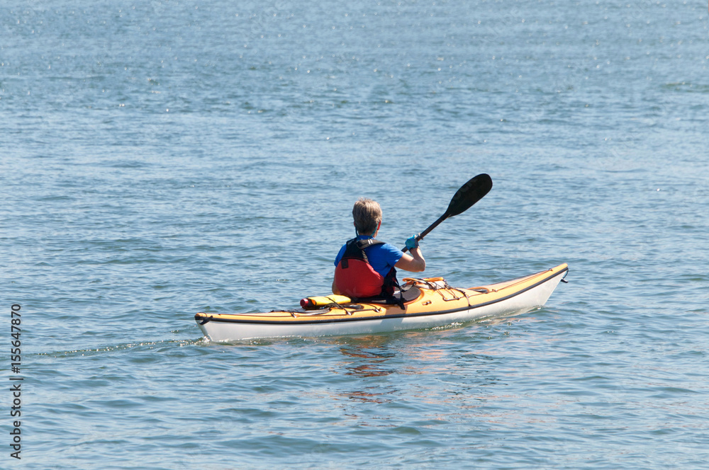 Lone kayak with older female paddling in open water away from viewer