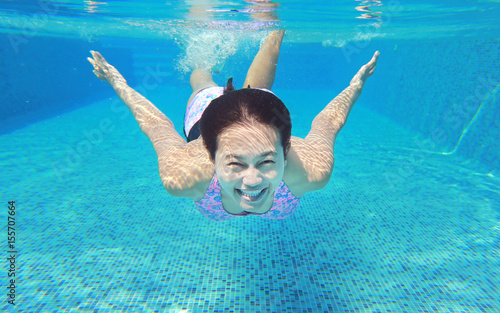 Underwater shot of young woman diving into the swimming pool.