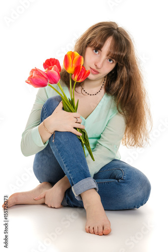 Attractive girl sitting on white floor with tulips in hand