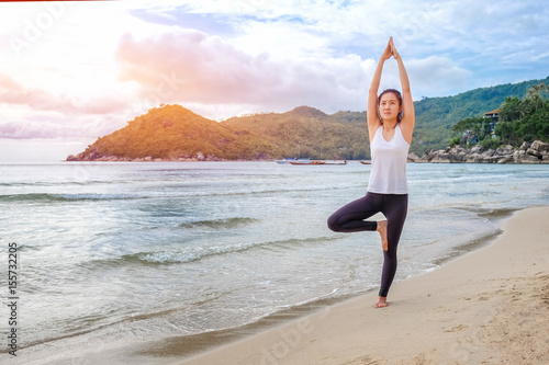 Young beautiful woman practicing yoga on the beach at sunrise..