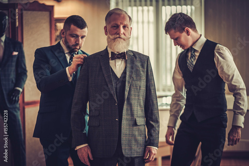 Φωτογραφία Tailor and his protege measuring client for custom made garment
