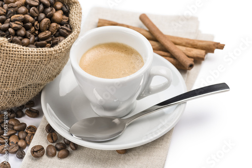 cup of coffee on napkin with canvas bag full of coffee beans and cinnamon, on white background