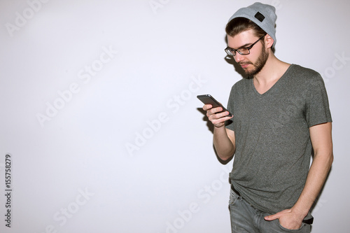 Hipster read text message on phone. Communication, friendship, social network concept. Man in gray casual cloth standing on white background with smartphone © Photodrive