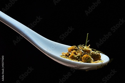 Flower heads and stalks of Chamomile Matricaria chamomilla on wooden laddle held in left male hand on dark background photo