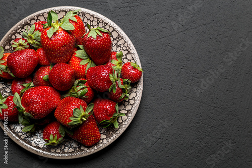 fresh ripe useful fruit strawberry in a clay bowl closeup on a black background