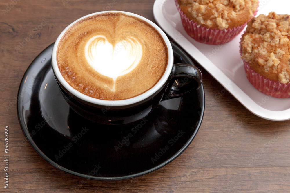 Coffee cup of latte art heart shape beside with muffins on wooden background