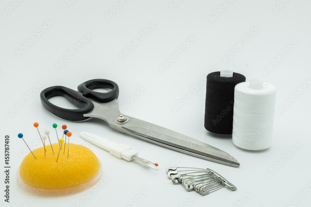 Scissor, seam ripper, sewing needle and threads over white background