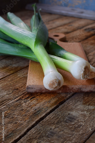 Freshly organic leeks on wooden background. Onion on cutting board