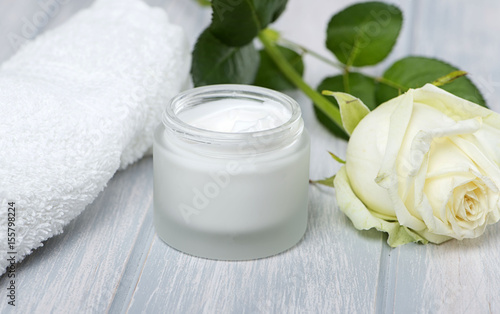 Close-up of a pot of cream for the skin  towel  white rose and almonds on wooden table.