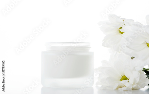 Close-up of daisy flowers and pot of cream for skin on white background. Isolated.