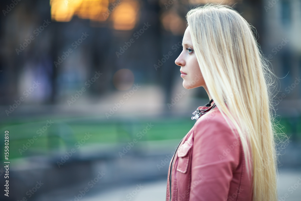 Profile portrait of young beautiful blond woman in city street on sunset