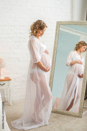 A young pregnant woman touching her belly in the mirror background photo