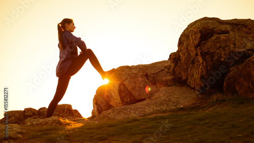 Young Fitness Woman Stretching her Legs in the Mountains at Sunset. Female Runner Doing Stretches Outdoor. Healthy Lifestyle Concept.