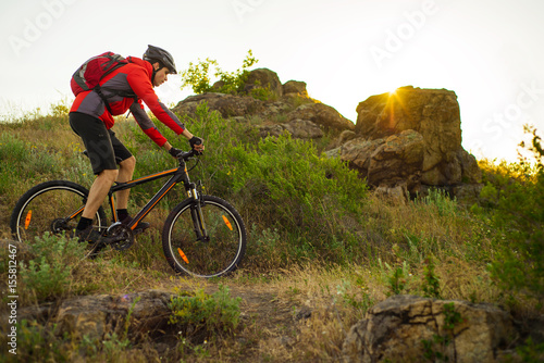 Cyclist in Red Jacket Riding the Mountain Bike on the Beautiful Spring Rocky Trail at Sunset. Adventure and Extreme Sport Concept