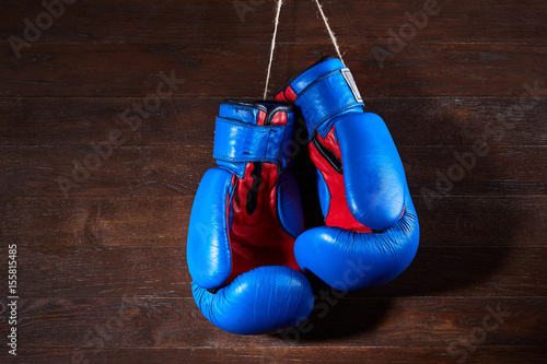 A pair of bright blue and red boxing gloves hangs against wooden background. © Aleksey