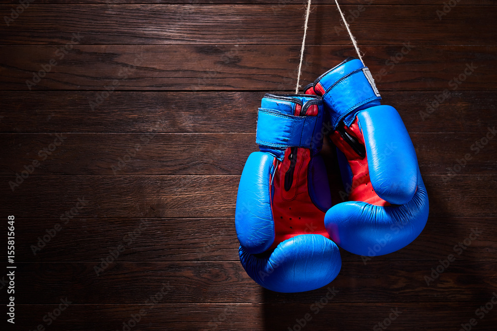 A pair of bright blue and red boxing gloves hangs against wooden background.