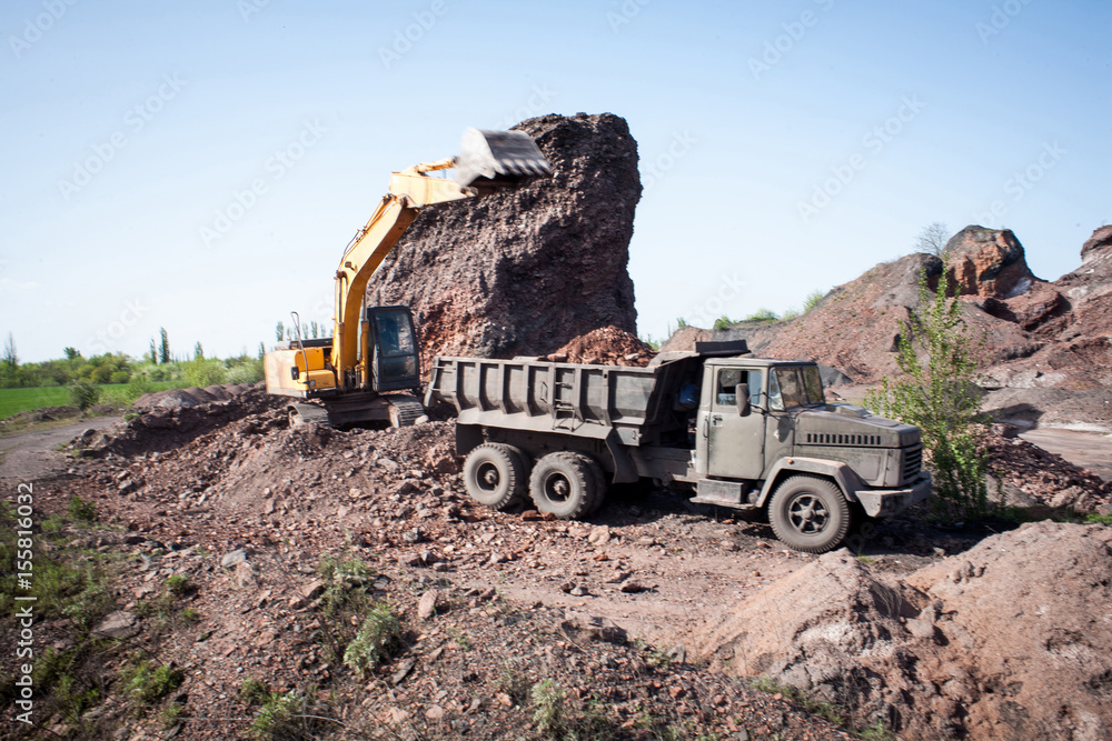 Excavator poured cargo into the body of a quarry truck for transportation to the construction site