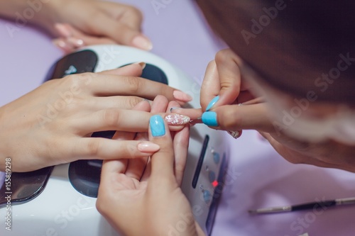 Manicure in the spa salon. Drawing of nail polish. Spa manicure, nail care. Girl does a manicure. The concept of hand care.