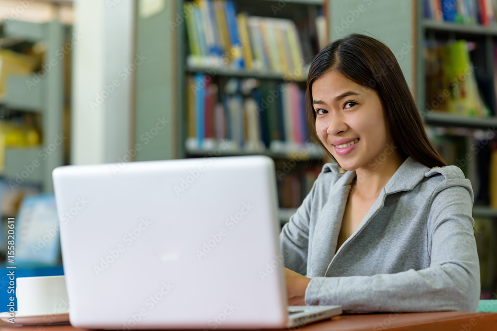 Beautiful Asian businesswoman is using a laptop computer on a wooden desk in an office library. Finance, Banking and Technology Concepts. Beautiful Asian businesswoman is using a laptop computer on a wooden desk in an office library. Finance, Banking and Technology Concepts.