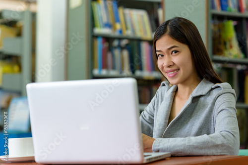 Beautiful Asian businesswoman is using a laptop computer on a wooden desk in an office library. Finance, Banking and Technology Concepts.