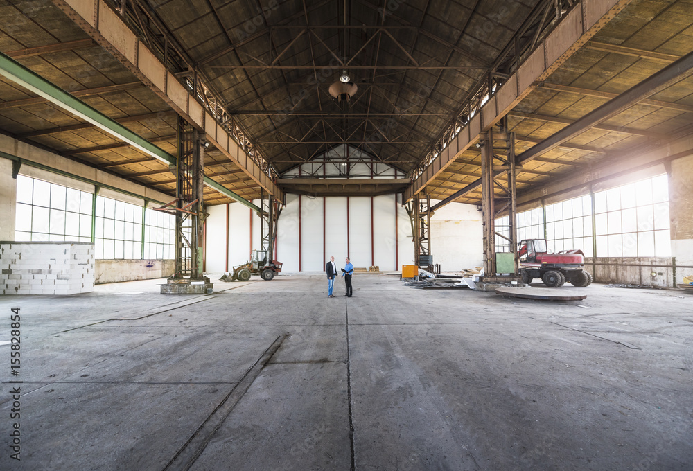Two businessmen with documents talking in old industrial hall Two businessmen with documents talking in old industrial hall