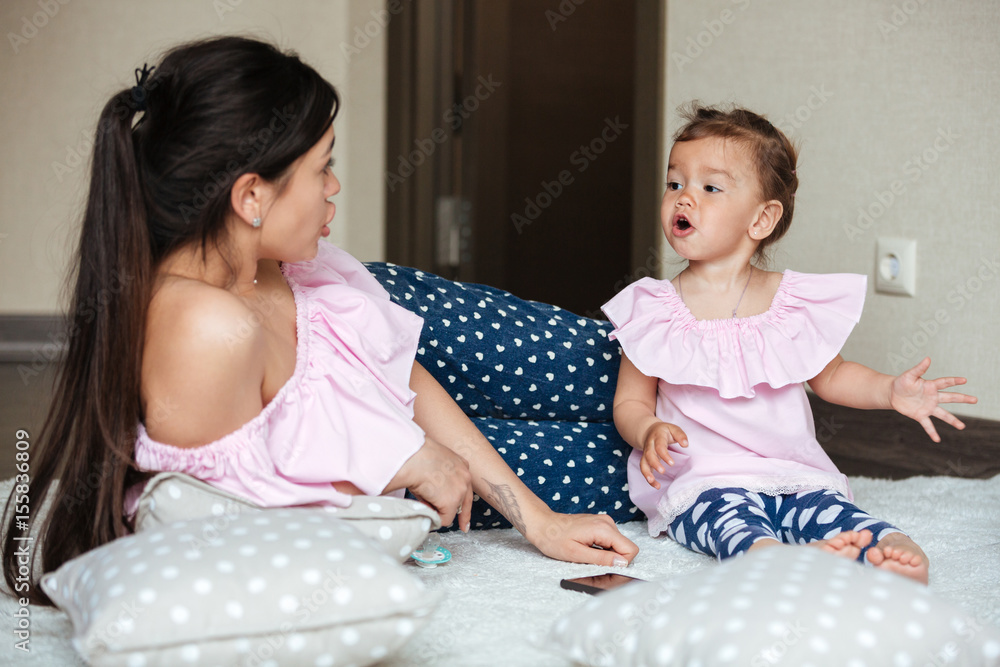 Beautiful young mother with her little daughter lies on bed Beautiful young mother with her little daughter lies on bed