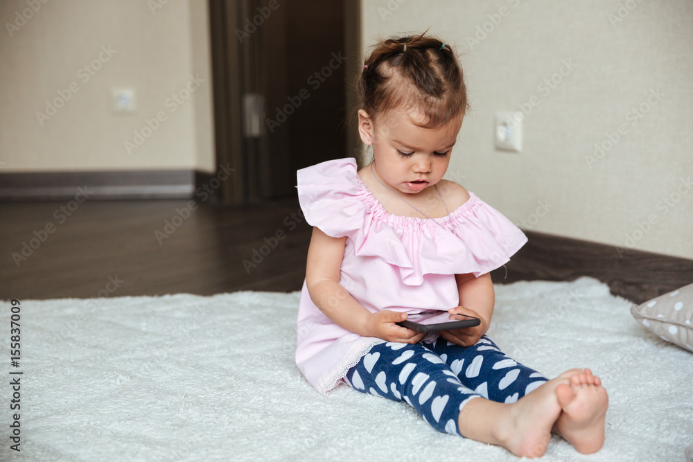 Concentrated little girl child sitting on bed using phone Concentrated little girl child sitting on bed using phone