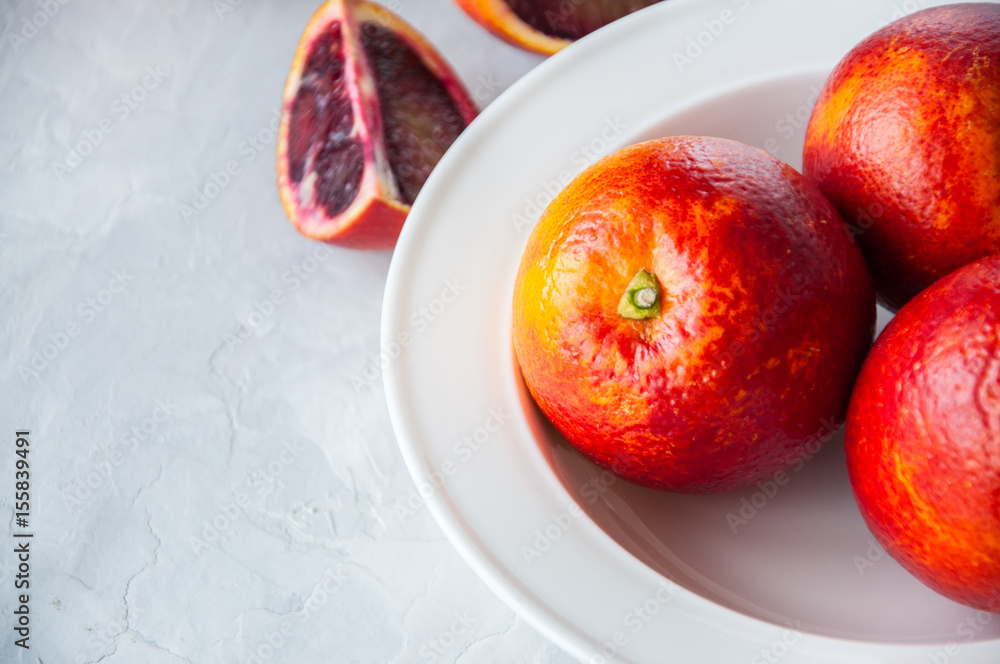 Fresh ripe whole and slices of blood oranges in a plate on a white stone background. Copy space and close up. Fresh ripe whole and slices of blood oranges in a plate on a white stone background. Copy space and close up.