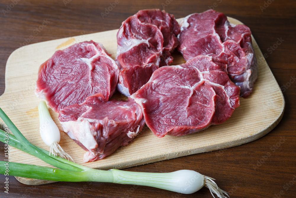 Raw beef slices on a cutting board with a spring onion Raw beef slices on a cutting board with a spring onion