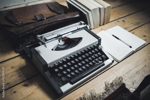A vintage gray typewriter on a wooden floor. Notepad, pen, books and leather briefcase on the wooden floor